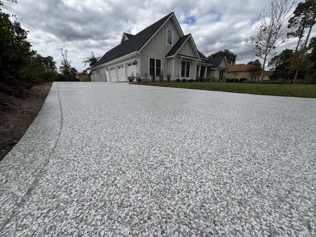 Decorative concrete driveway with textured finish leading to a modern house with a large garage and well-maintained lawn.