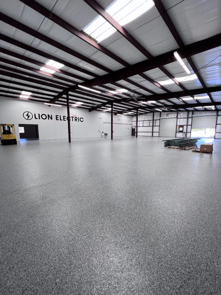 Spacious industrial warehouse with polished epoxy flooring and high metal ceiling, featuring the Lion Electric logo on the wall.
