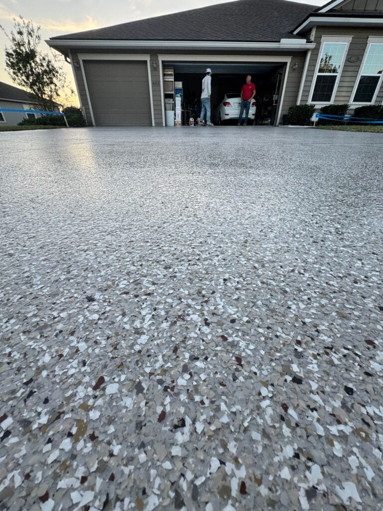 Freshly coated concrete driveway with a textured finish in front of a modern house with an open garage.
