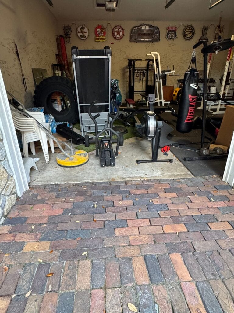 Home gym setup with workout equipment in a garage, including weights, punching bag, and exercise machines.