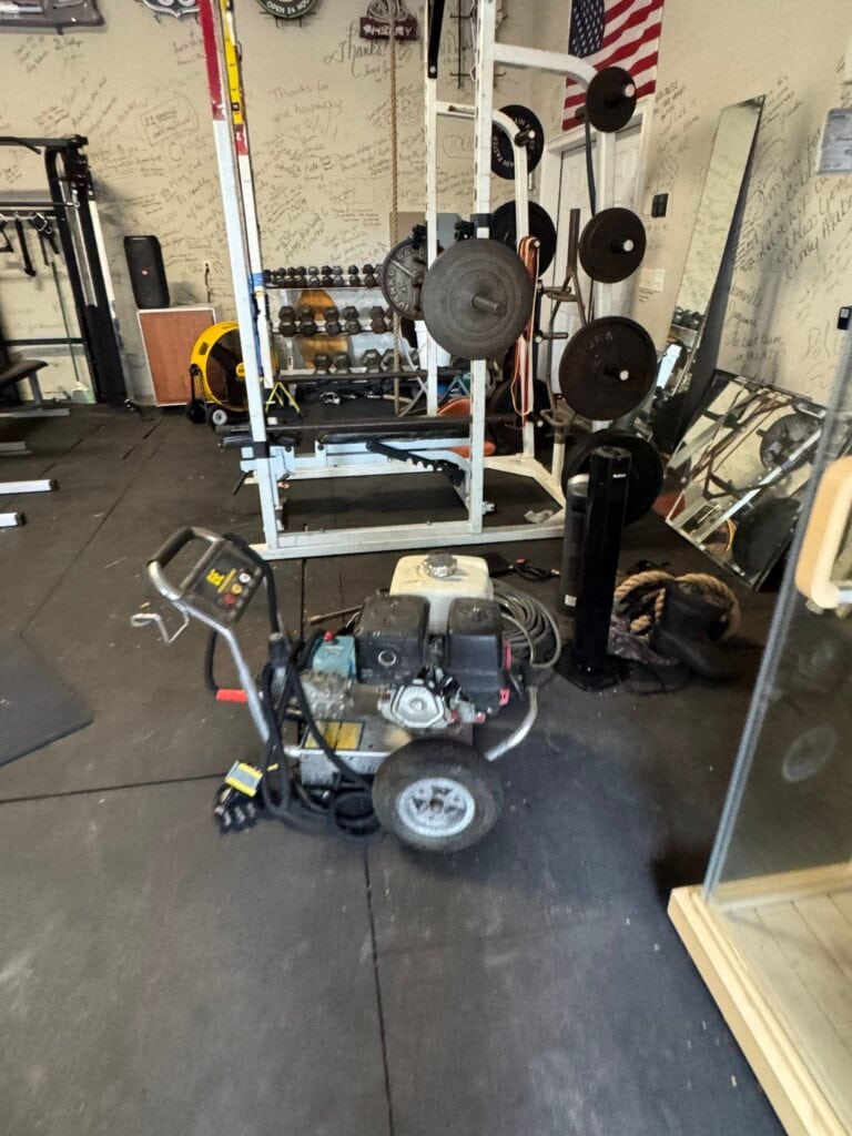 Garage gym with weightlifting equipment, mirrors, and a floor cleaning machine in a Jax-based space.