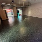 Empty garage gym with speckled polyaspartic flooring, white walls, and open garage doors in Jacksonville.