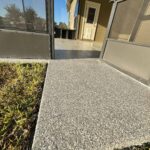 Concrete patio with textured finish at residence, featuring a screened porch and door, under a clear blue sky.