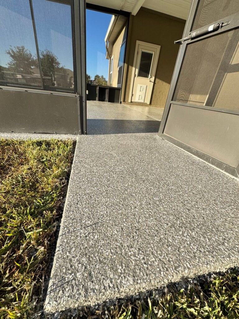Concrete patio with textured finish at residence, featuring a screened porch and door, under a clear blue sky.