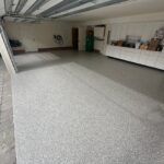 Garage floor with durable, speckled polyaspartic coating in a residential garage, featuring white cabinets and organized storage.