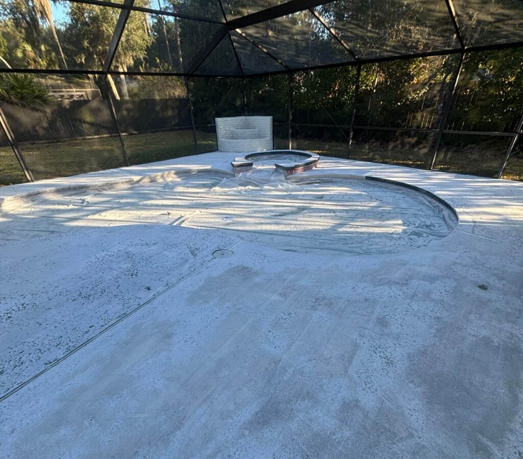Concrete pool deck, surrounded by a screened enclosure and lush greenery in the background.