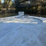Concrete pool deck, surrounded by a screened enclosure and lush greenery in the background.