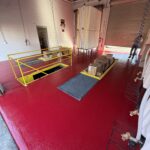 Industrial coating facility with red polyaspartic floor, safety railing, and equipment for automotive or industrial applications.