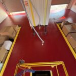 Checkmate Coatings polyaspartic flooring in a garage with a vehicle lift and storage boxes, showcasing durable, high-quality surface protection.