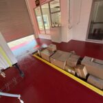 Boxes of supplies inside Checkmate Coatings facility with red flooring and large garage door.