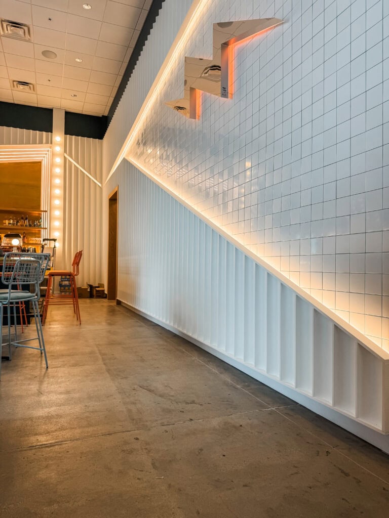 Modern interior design with white tiled wall, ambient lighting, and seating area in a contemporary restaurant.