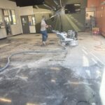 Worker cleaning the floor at Checkmate Coatings with industrial equipment in a commercial space.