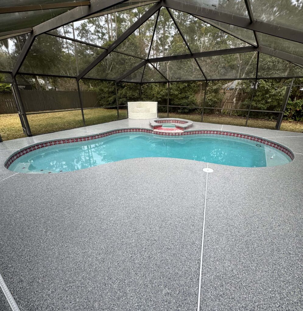 Pool deck with stonewash finish surrounding a swimming pool, enclosed by a screened patio with trees in the background.