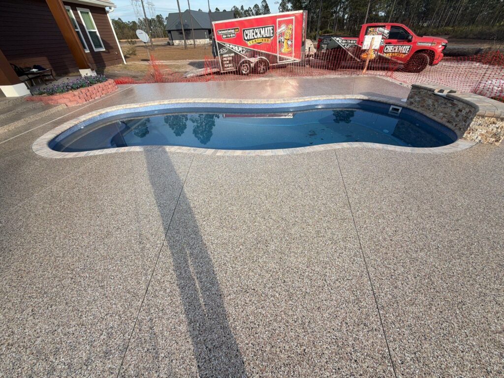 Newly installed backyard pool with textured concrete deck and stone border, under construction with a Chekmate Coatings project.