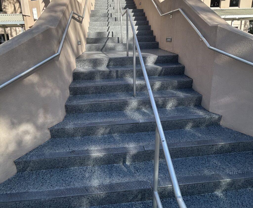 Concrete outdoor staircase with metal handrails leading up to a building, illuminated by sunlight.