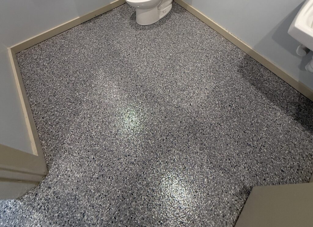 Close-up of a stonewashed epoxy floor in a restroom, showcasing durable, textured surface with speckled gray and black finish.