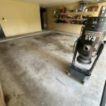 Prepping garage floor for professional coating, featuring a concrete surface and storage shelves in the background.