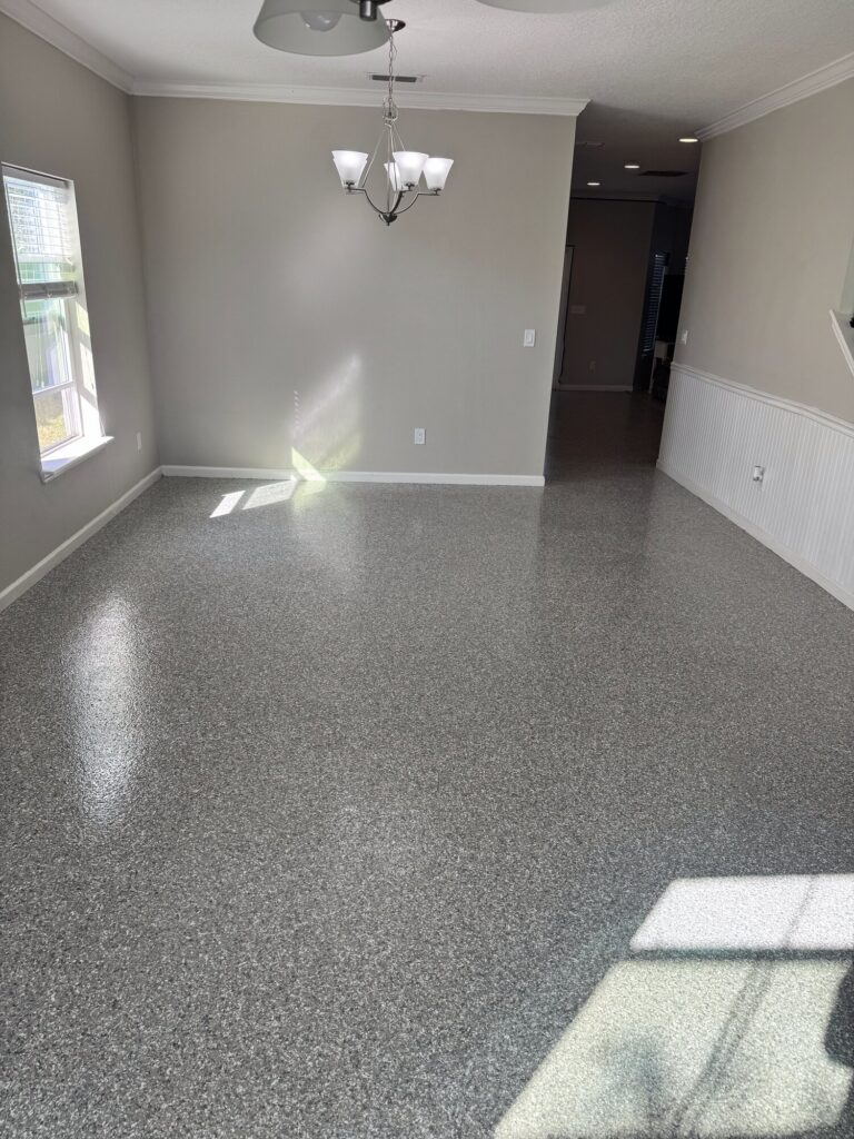 Interior room with newly coated speckled flake flooring, bright natural light, and modern chandelier, showcasing durable and stylish surface.